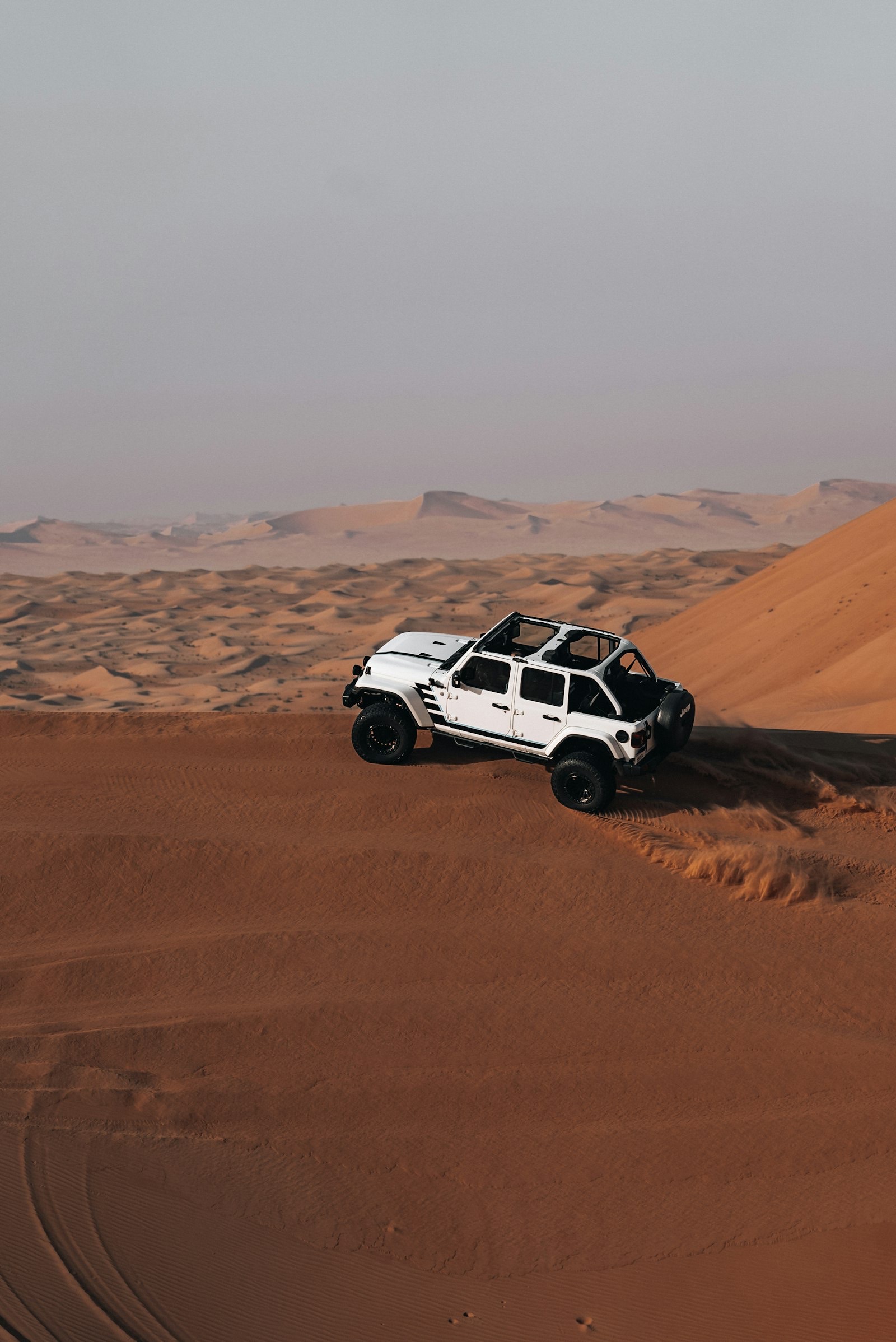 Open-top off-road vehicle cresting reddish desert sand dunes