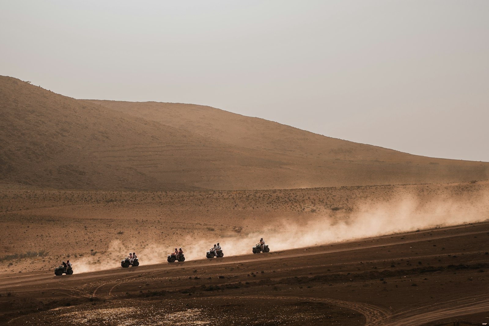 Line of ATVs kicking up dust across arid desert hills