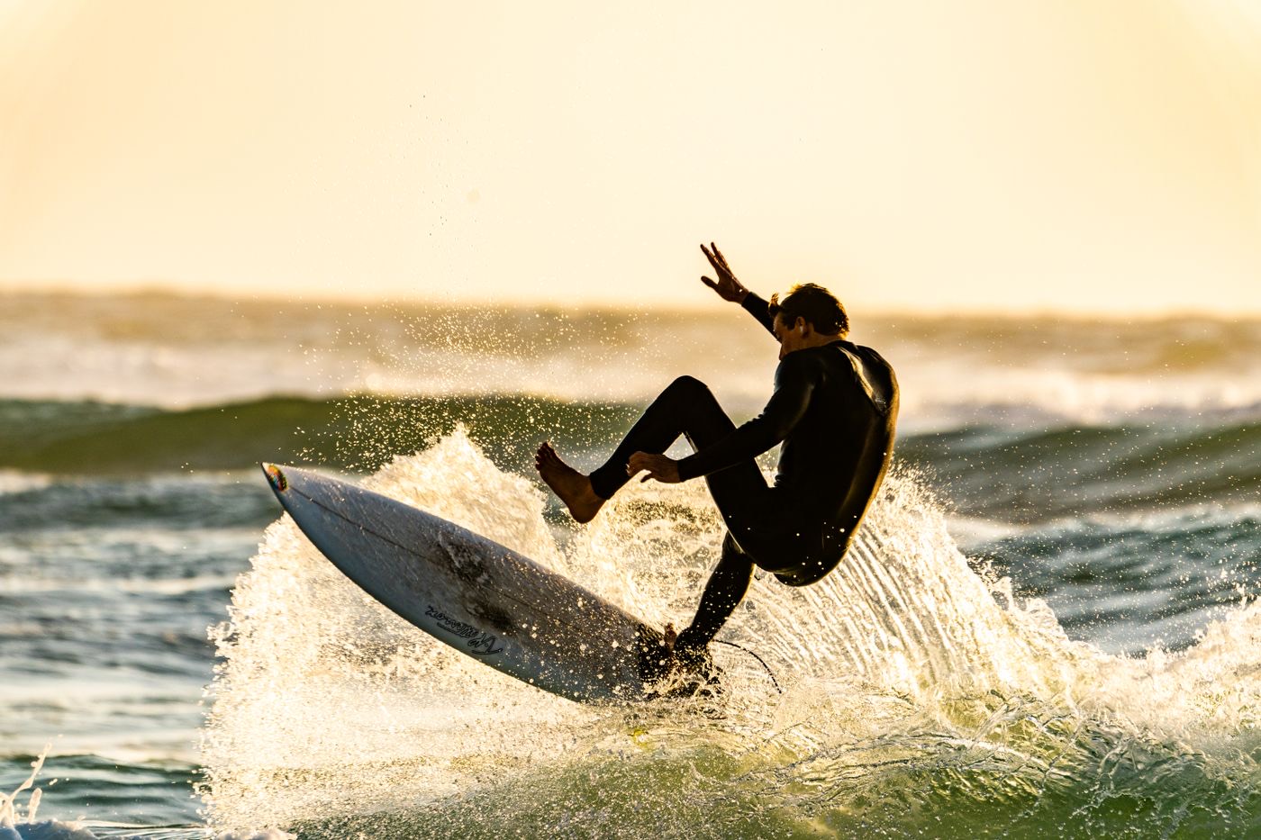 Surfer launching off a wave crest in golden backlight