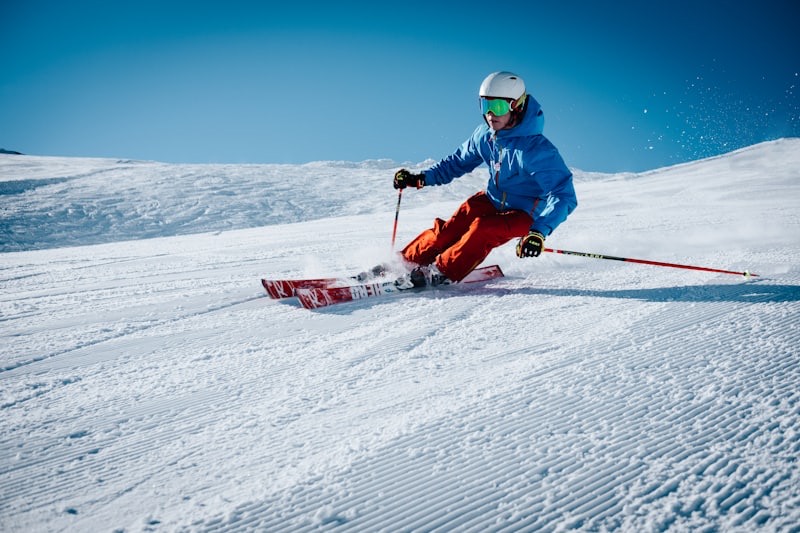 Skier carving a groomed run under a clear blue sky