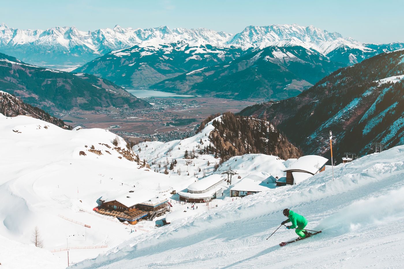 Skier in green suit carving above an alpine resort valley